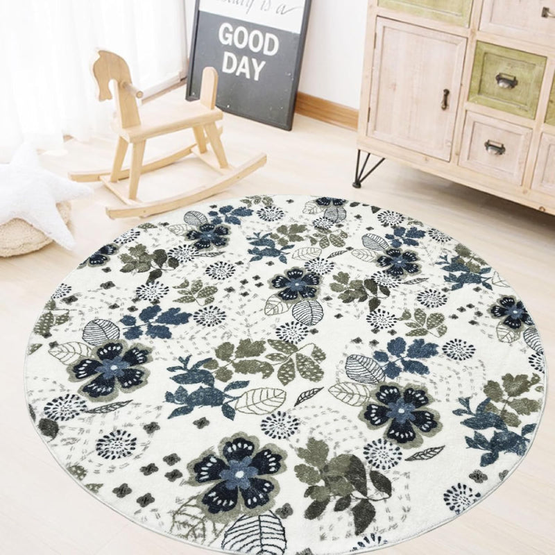 Round living room rug with blue and green floral pattern on an ivory background, placed in a cozy wooden interior with a rocking horse and storage cabinet.