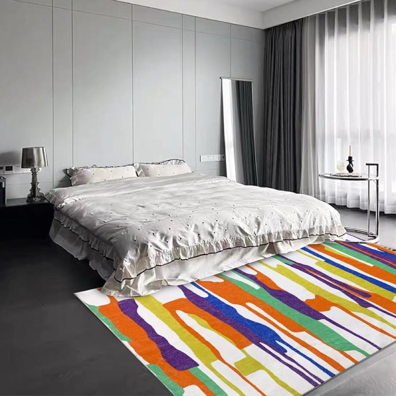 Modern living room with a neutral-tone multicolor block area rug featuring abstract horizontal stripes in gray, white, green, and black tones, placed on a wooden floor with cozy furniture and minimalist decor.