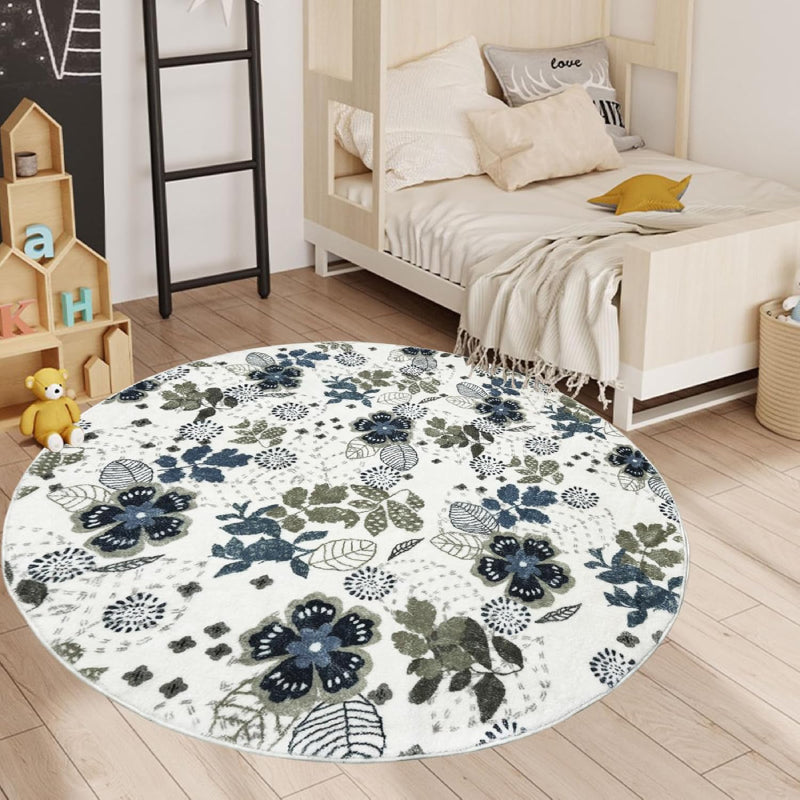 Round living room rug with blue and green floral pattern on an ivory background, placed in a cozy wooden interior with a rocking horse and storage cabinet.