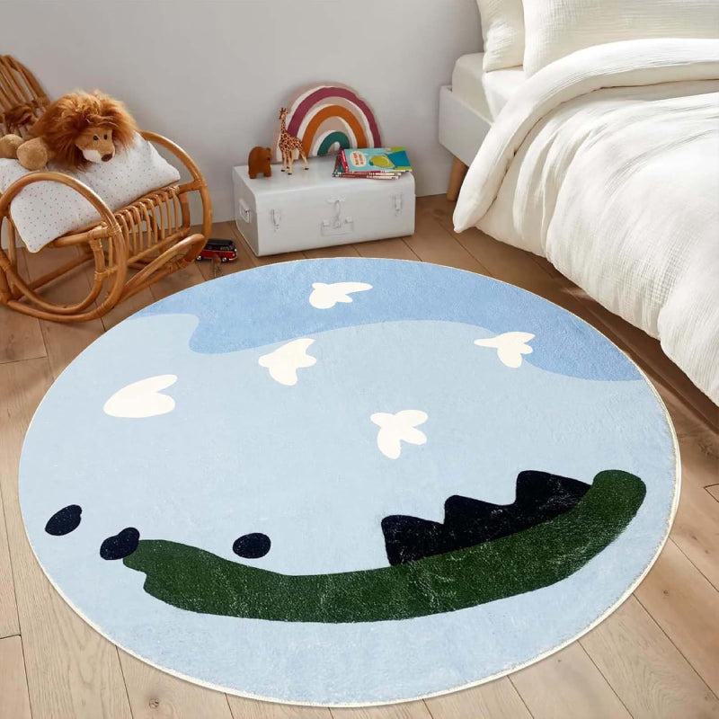 Round kids rug featuring a whimsical sky scene with light blue and dark blue abstract clouds, white cartoon-style birds flying, and green and black land-like shapes at the bottom on a soft background.