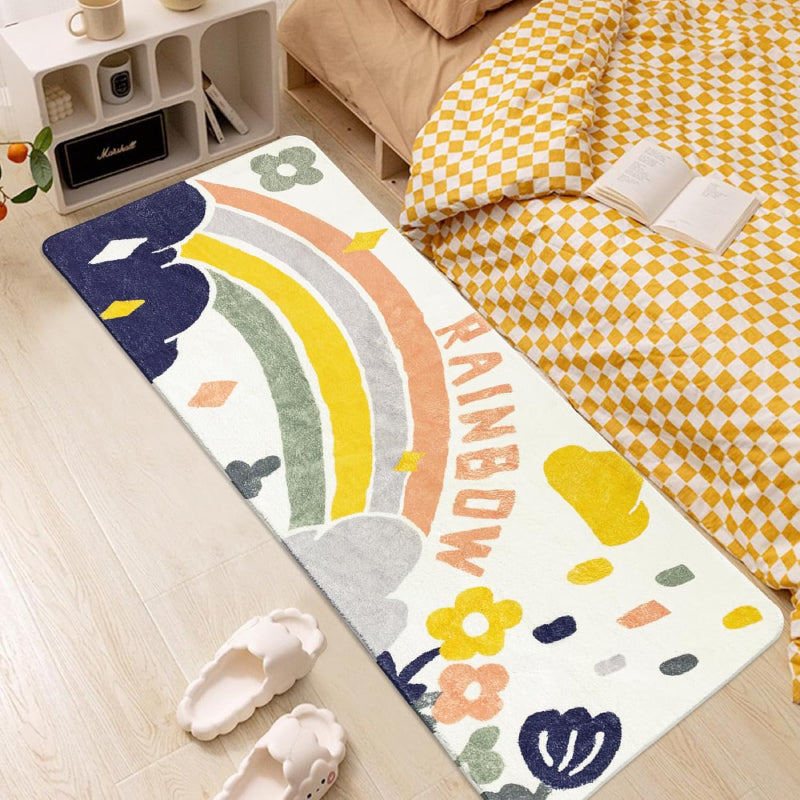 Colorful rectangular kids rug featuring a hand-drawn rainbow, clouds, raindrops, flowers, and the word "RAINBOW" in playful letters, placed in a cozy playroom setting.