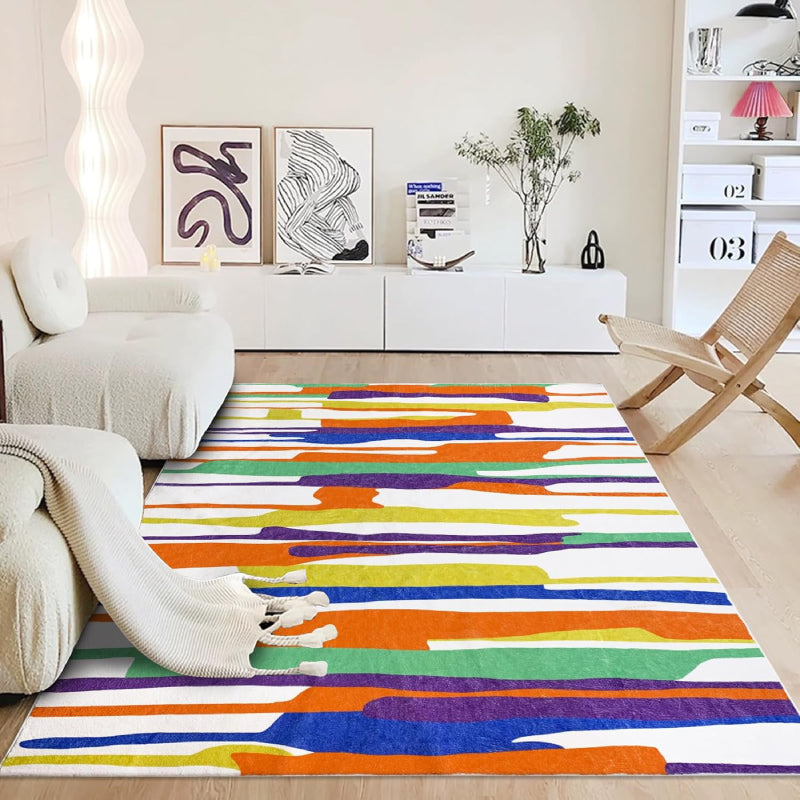 Modern living room with a neutral-tone multicolor block area rug featuring abstract horizontal stripes in gray, white, green, and black tones, placed on a wooden floor with cozy furniture and minimalist decor.