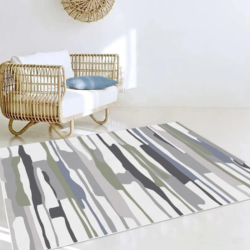 Modern living room with a neutral-tone multicolor block area rug featuring abstract horizontal stripes in gray, white, green, and black tones, placed on a wooden floor with cozy furniture and minimalist decor.