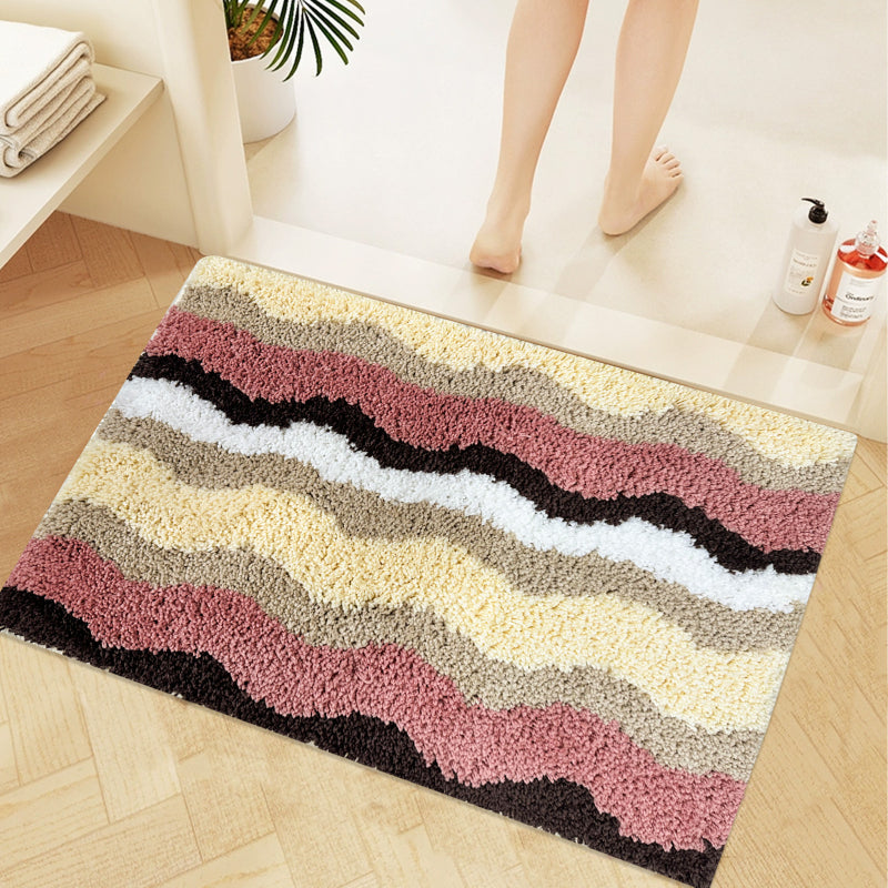 Rectangular bathroom rug with a wavy stripe pattern in pink, yellow, beige, brown, and white, featuring a soft and plush texture.