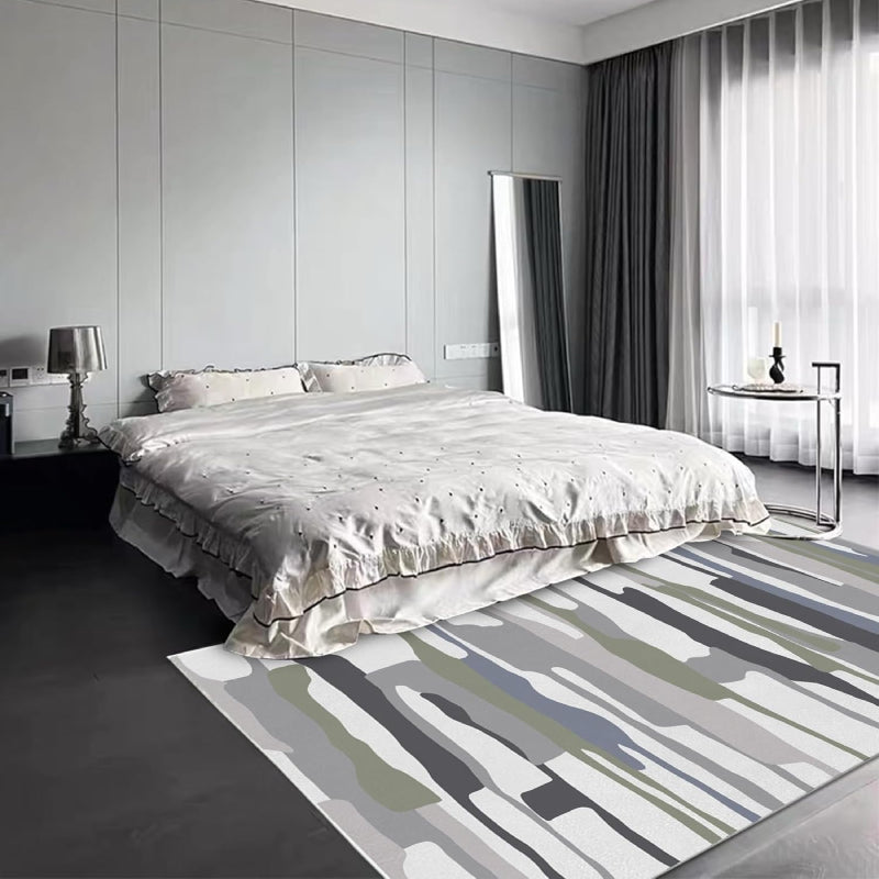 Modern living room with a neutral-tone multicolor block area rug featuring abstract horizontal stripes in gray, white, green, and black tones, placed on a wooden floor with cozy furniture and minimalist decor.