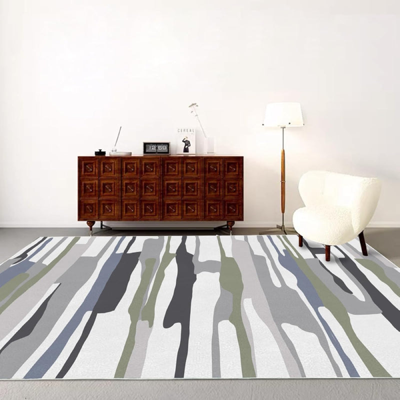 Modern living room with a neutral-tone multicolor block area rug featuring abstract horizontal stripes in gray, white, green, and black tones, placed on a wooden floor with cozy furniture and minimalist decor.