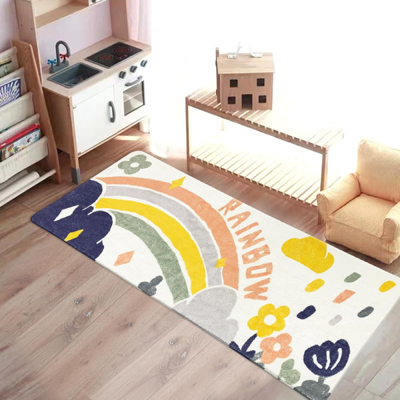 Colorful rectangular kids rug featuring a hand-drawn rainbow, clouds, raindrops, flowers, and the word "RAINBOW" in playful letters, placed in a cozy playroom setting.
