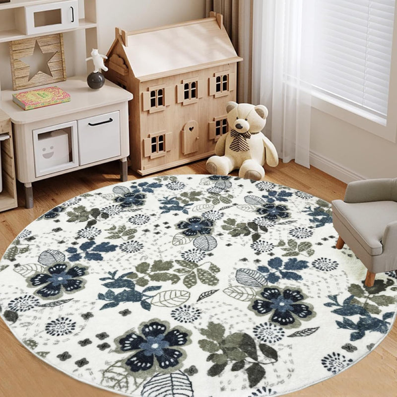 Round living room rug with blue and green floral pattern on an ivory background, placed in a cozy wooden interior with a rocking horse and storage cabinet.