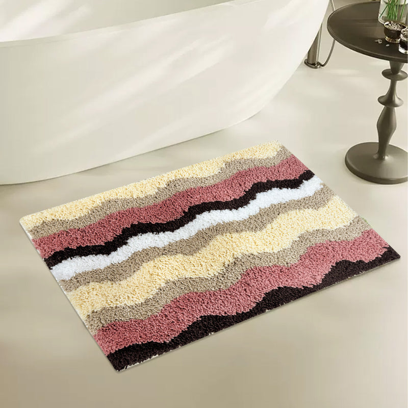 Rectangular bathroom rug with a wavy stripe pattern in pink, yellow, beige, brown, and white, featuring a soft and plush texture.